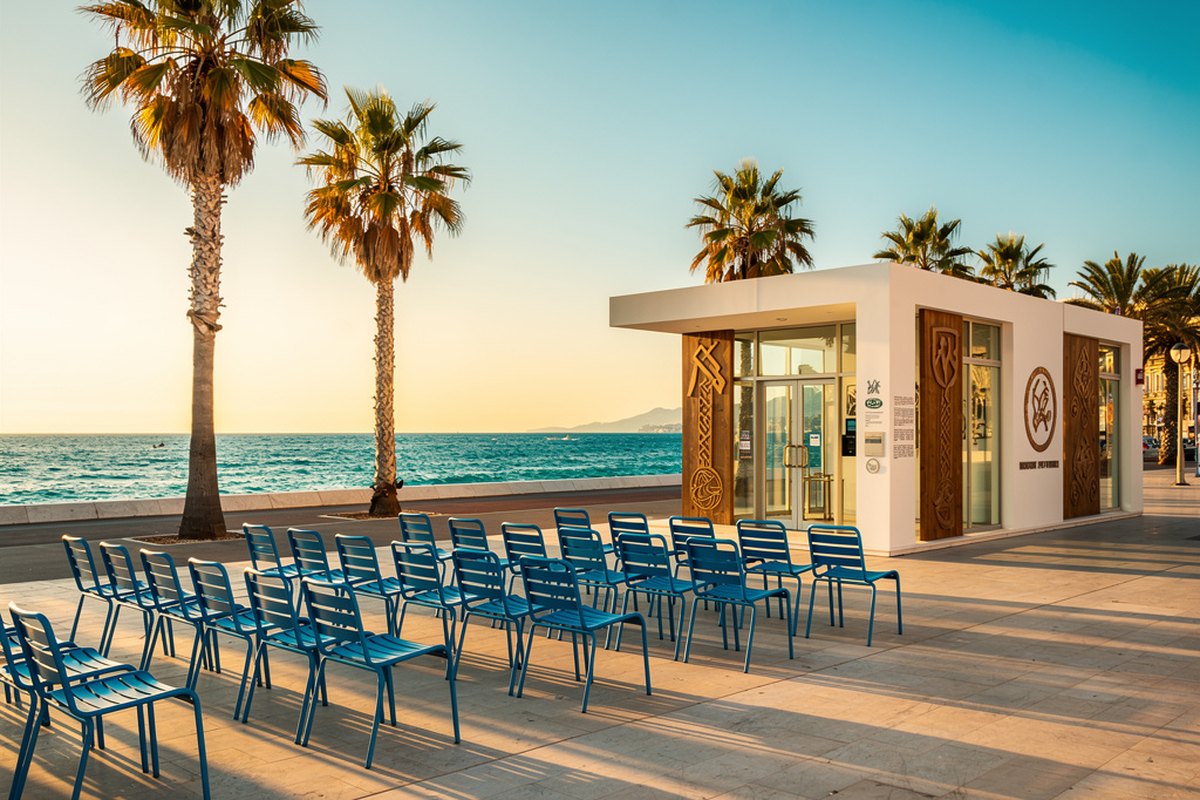 La Promenade des Anglais à Nice au coucher du soleil avec ses chaises bleues et palmiers face à la Méditerranée.