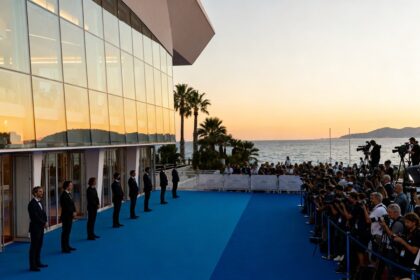 Tapis bleu et photographes devant un palais des congrès vitré en bord de Méditerranée au crépuscule