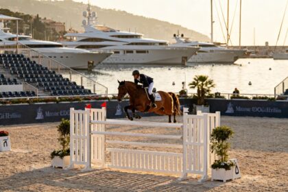 Cavalier et cheval franchissant un obstacle sur une piste de sable au bord du port de Monaco, yachts a l'arriere-plan.