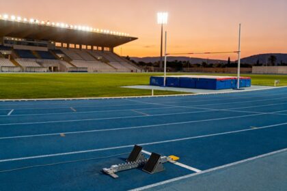 Piste d'athletisme bleue et aire de saut a la perche dans un stade illumine a la tombee du soir