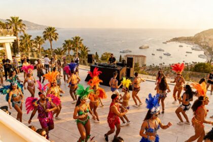 Danseurs en costumes à plumes colorées sur une terrasse dominant la mer au coucher du soleil