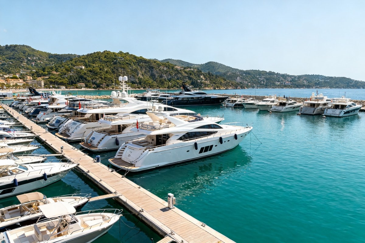 Yachts de luxe amarrés le long des pontons d'un port méditerranéen ensoleillé, collines verdoyantes en arrière-plan
