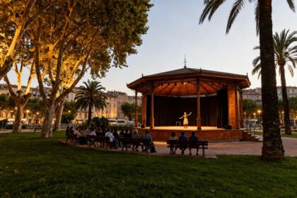 Kiosque de plein air dans un parc urbain, spectateurs assis face à une scène au crépuscule