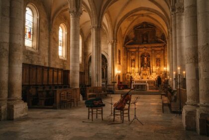 Intérieur d'une cathédrale en pierre à la lueur des bougies, un violoncelle et un violon posés près de l'autel