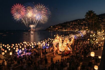 Feu d'artifice au-dessus d'une baie et parade illuminée en forme de dragon sur une promenade de bord de mer la nuit