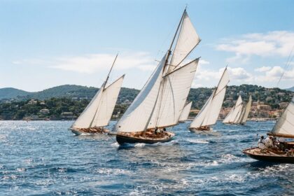 Voiliers classiques aux grandes voiles blanches en régate sur une baie méditerranéenne bordée de collines, par temps ensoleillé