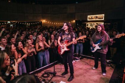 Deux jeunes musiciennes à la guitare et à la basse sur une petite scène, face à un public serré