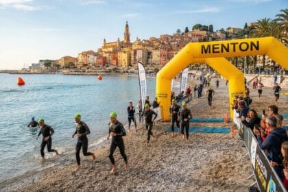 Nageurs en combinaison sortant de la mer sous une arche gonflable jaune, devant la vieille ville de Menton