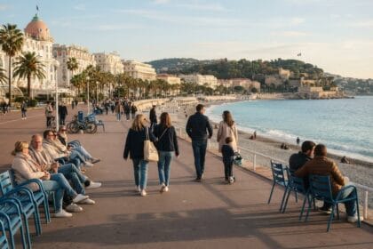Promeneurs en vestes légères et chaises bleues sur la Promenade des Anglais à Nice, face à la baie des Anges