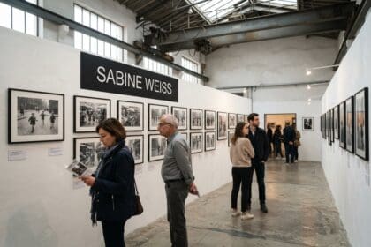 Visiteurs devant des tirages noir et blanc sous un panneau Sabine Weiss, dans une salle d'exposition aux poutres métalliques